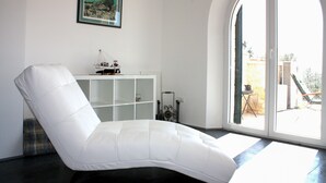 A white cushioned chair in a room with a large window, a white cabinet, and a framed picture on the wall. - Villa Aleksandra (Novigrad)