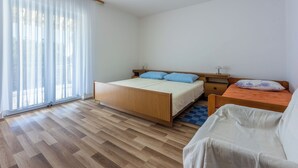 Egy hálószoba, amelyben egy faágy, egy kis asztal, egy szék és egy vékony, áttetsző függönnyel ellátott ablak található.