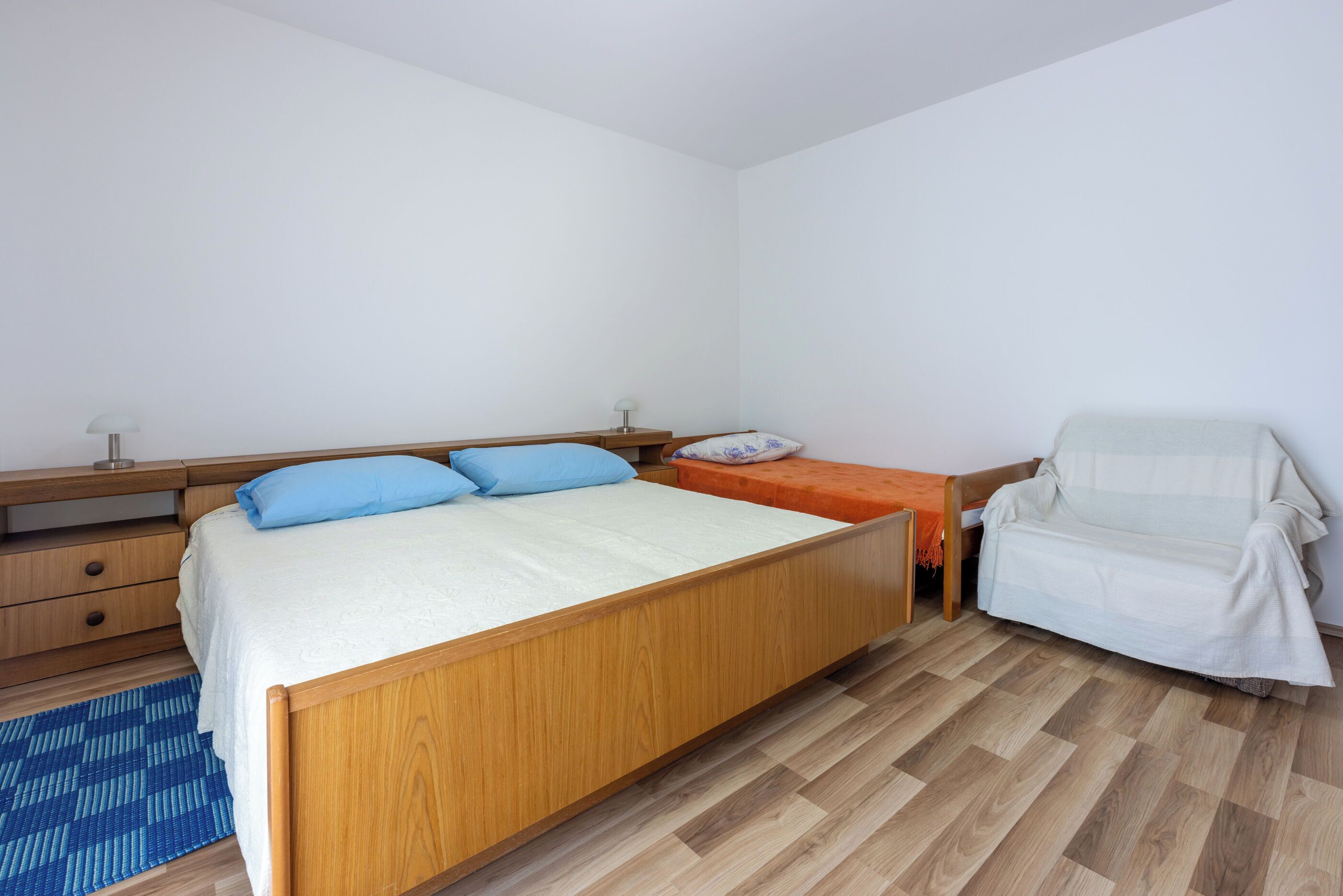 Quarto com cama de madeira, mesa de cabeceira, cadeira e tapete azul estampado.