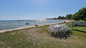 A poolside area with white chairs and a table, overlooking a body of water with boats and people. - Villa Rafajela (Privlaka)