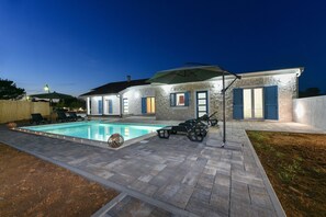 A swimming pool with lounge chairs and umbrellas, surrounded by stone walls and a covered patio area. - Villa Rafajela (Privlaka)