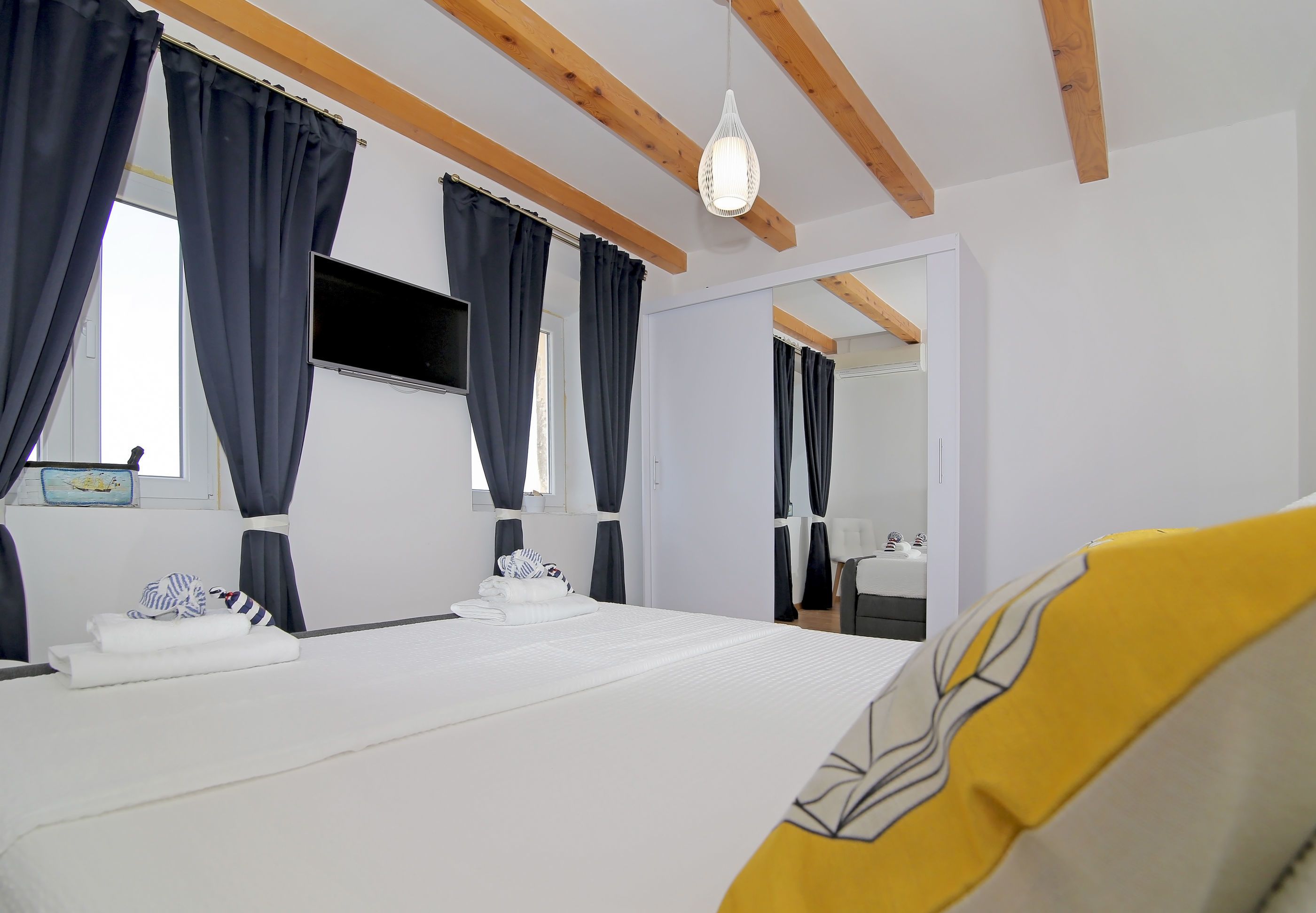 A hotel room with a bed, curtains, a TV, and a mirror.