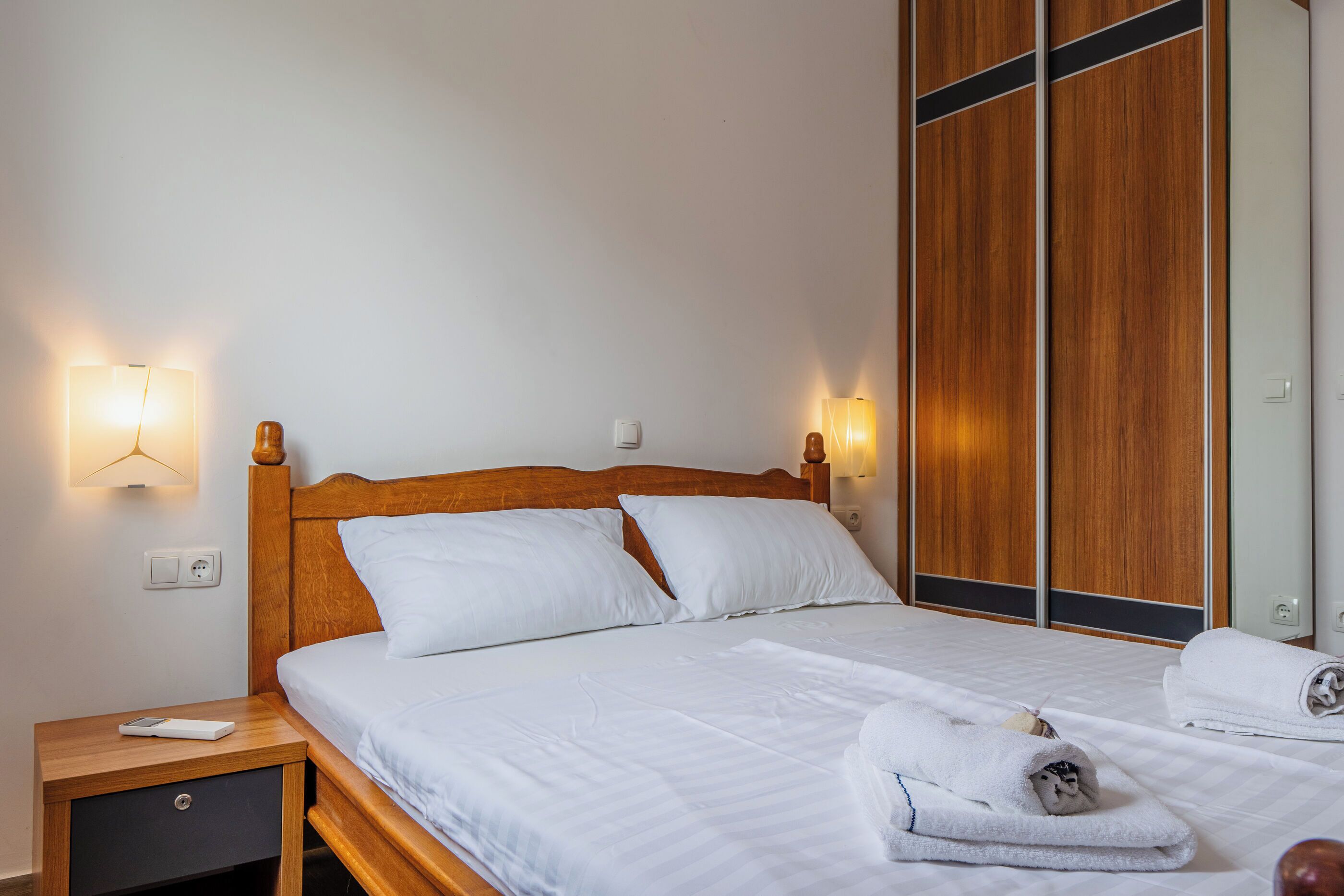 A neatly made bed with white linens, a wooden headboard, and two bedside lamps.
