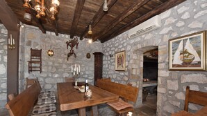 A rustic stone-walled room with a wooden dining table, benches, and a fireplace. - House La Casa Simone (Jesenice)