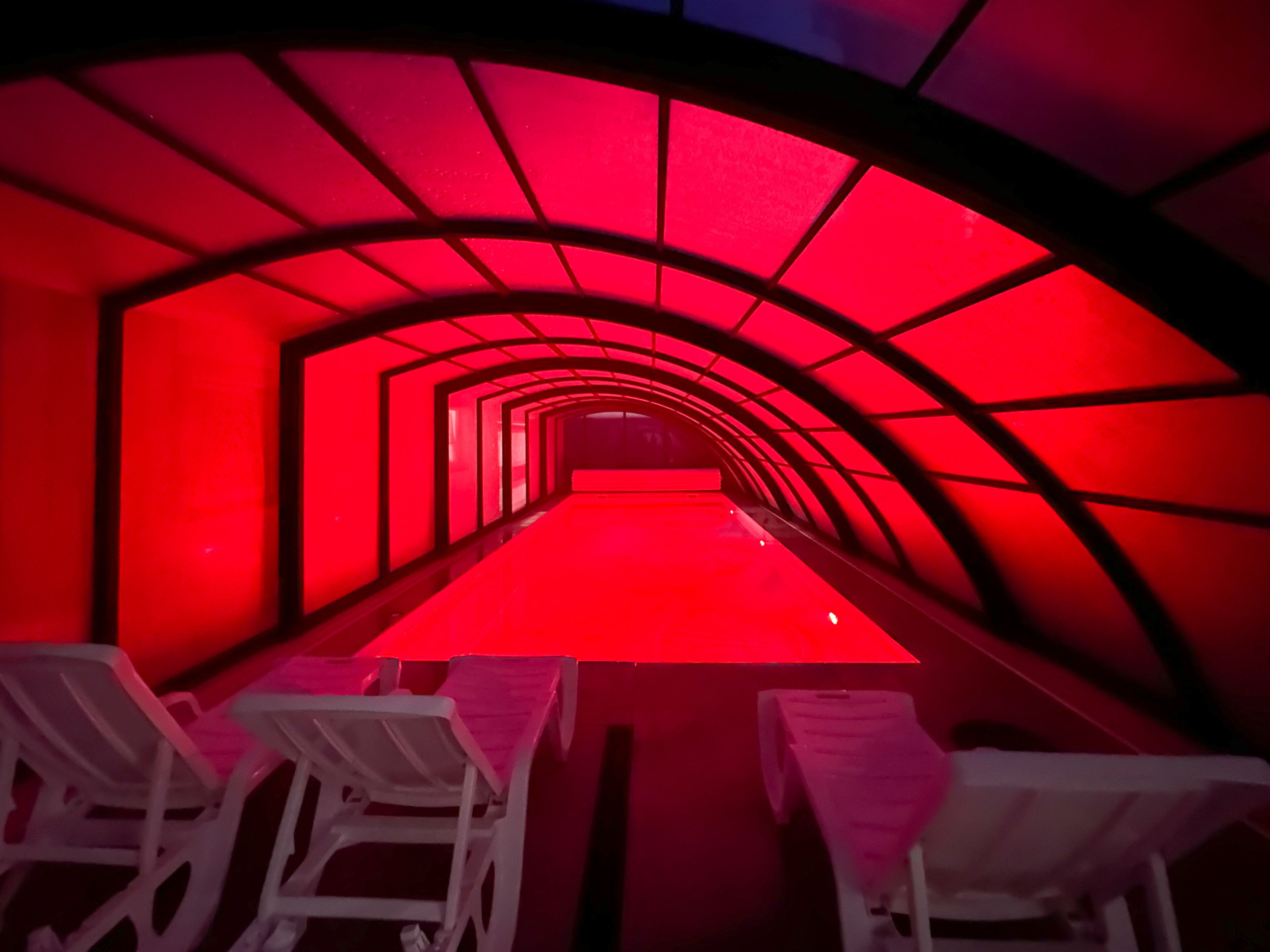 Una estructura en forma de túnel con iluminación roja y sillas blancas dispuestas a lo largo de los lados.