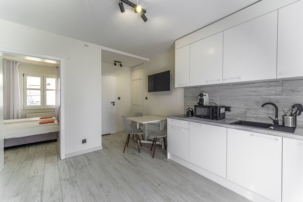 A modern kitchen with white cabinets, a built-in microwave, and a sink. There is a dining area with a table and chairs.