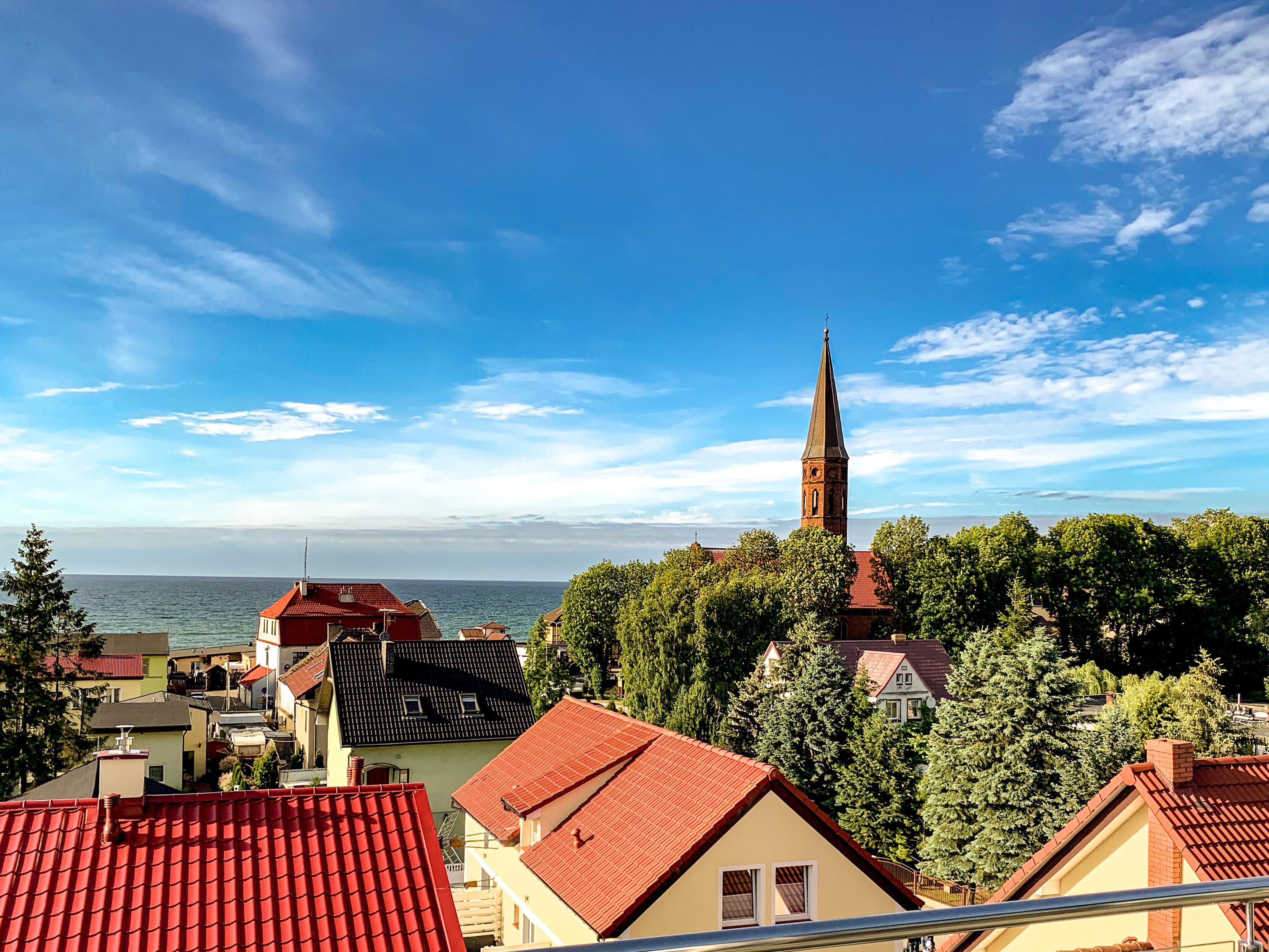 A coastal town with a prominent church tower, surrounded by residential buildings with red-tiled roofs, and a view of the sea.