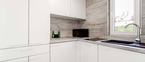 A modern kitchen with white cabinets, a built-in microwave, and a window with a view of a house.