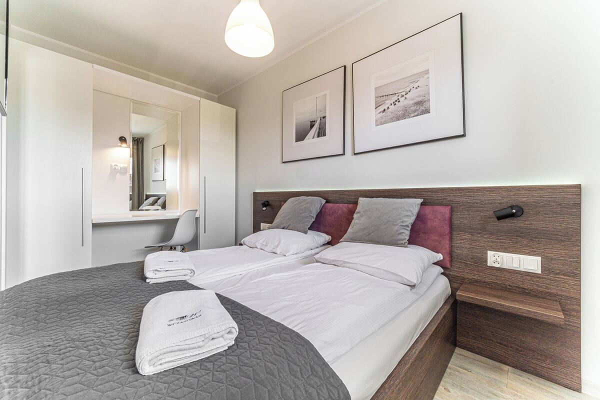 A hotel room with a large bed, a bedside table, a mirror, and two framed pictures on the wall.
