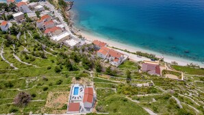 Oversigtsbillede af et kystnært boligområde med huse, en strand og en swimmingpool.