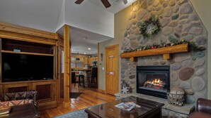 A cozy living room with a stone fireplace, wooden furniture, and a television.