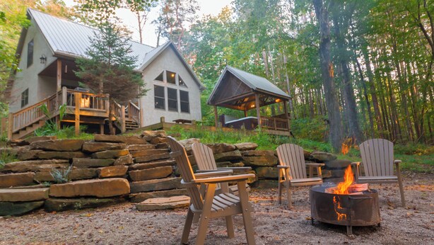 A cabin with a stone staircase, a fire pit, and two Adirondack chairs.