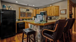 A kitchen with wooden cabinets, a black refrigerator, a stone island, and leather bar stools.