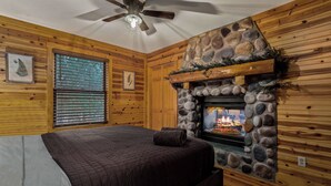 A cozy log cabin bedroom with a stone fireplace, a bed with a quilted blanket, and wooden walls.