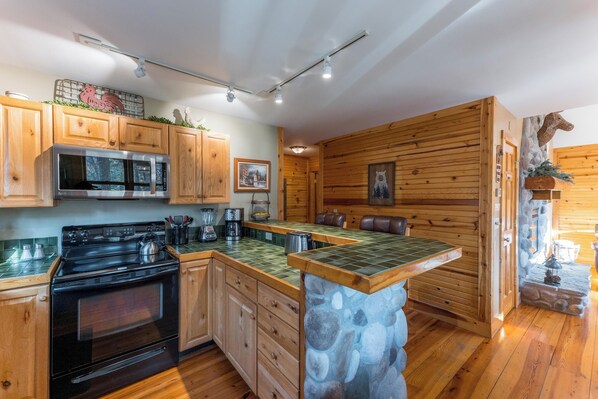 Una cocina con armarios de madera, estufa, microondas y una isla de piedra.