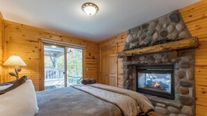 A cozy log cabin bedroom with a stone fireplace, wooden walls, and a large bed.