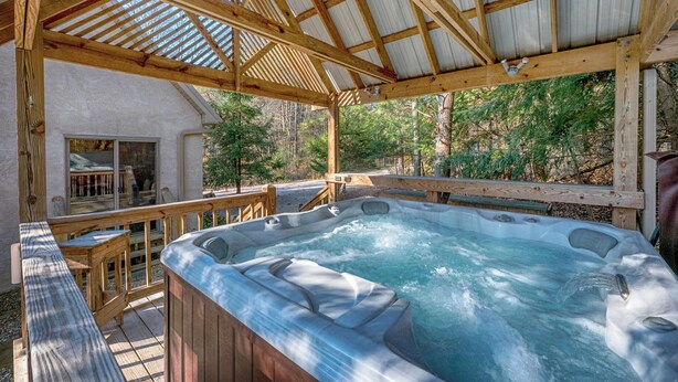 A wooden deck with a hot tub, wooden railings, and a covered area with a metal roof.