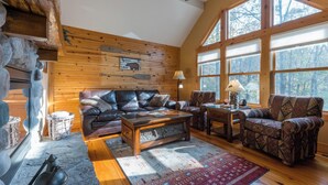 A cozy cabin interior with a wooden interior, leather furniture, and large windows offering a view of the forest.