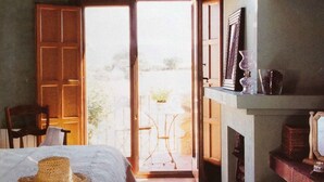 A cozy room with a bed, a chair, a fireplace, and a door leading to an outdoor area. - Casa Rota (Arahuetes)