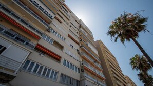 A multi-story residential building with balconies, a palm tree, and a clear sky. - Apartamento Paseo Maritimo 27 (Cádiz)