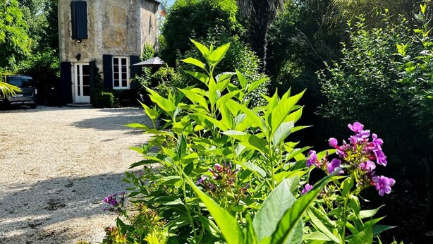 A rustic stone building with a tiled roof, surrounded by lush greenery and flowering plants. - Gîte La Folie de Labahou (Anduze)