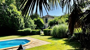 A swimming pool surrounded by well-maintained grass and hedges, with a lamp post and a small building in the background. - Gîte La Folie de Labahou (Anduze)