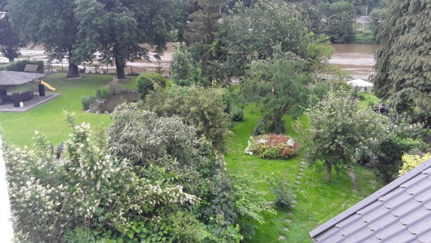 A lush garden with a gazebo, a river, and a mountainous backdrop.