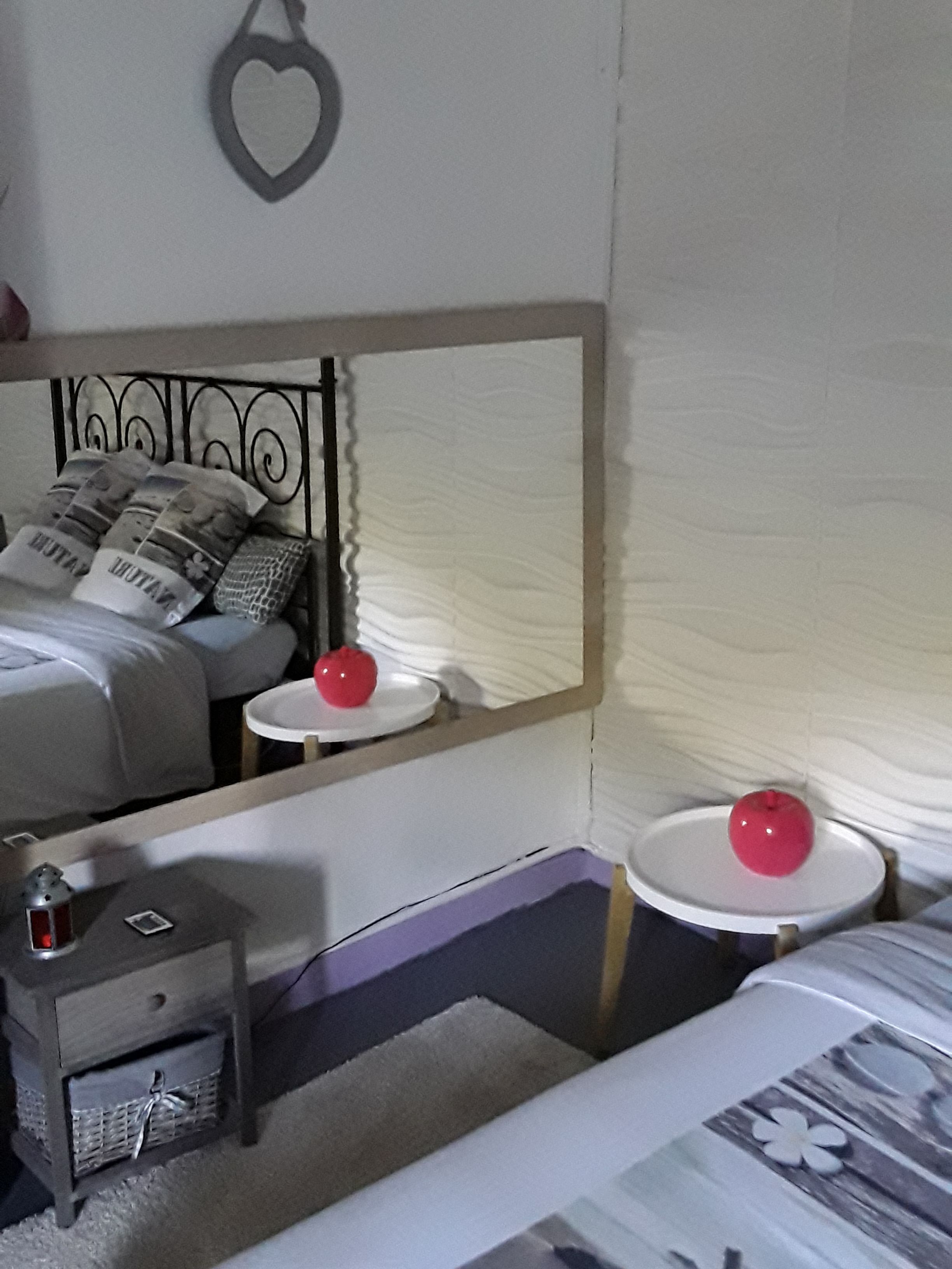 A bedroom with a bed, bedside tables, a mirror, and a wall-mounted heart-shaped decoration.