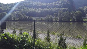 A chain-link fence with a river and a forested hill in the background.