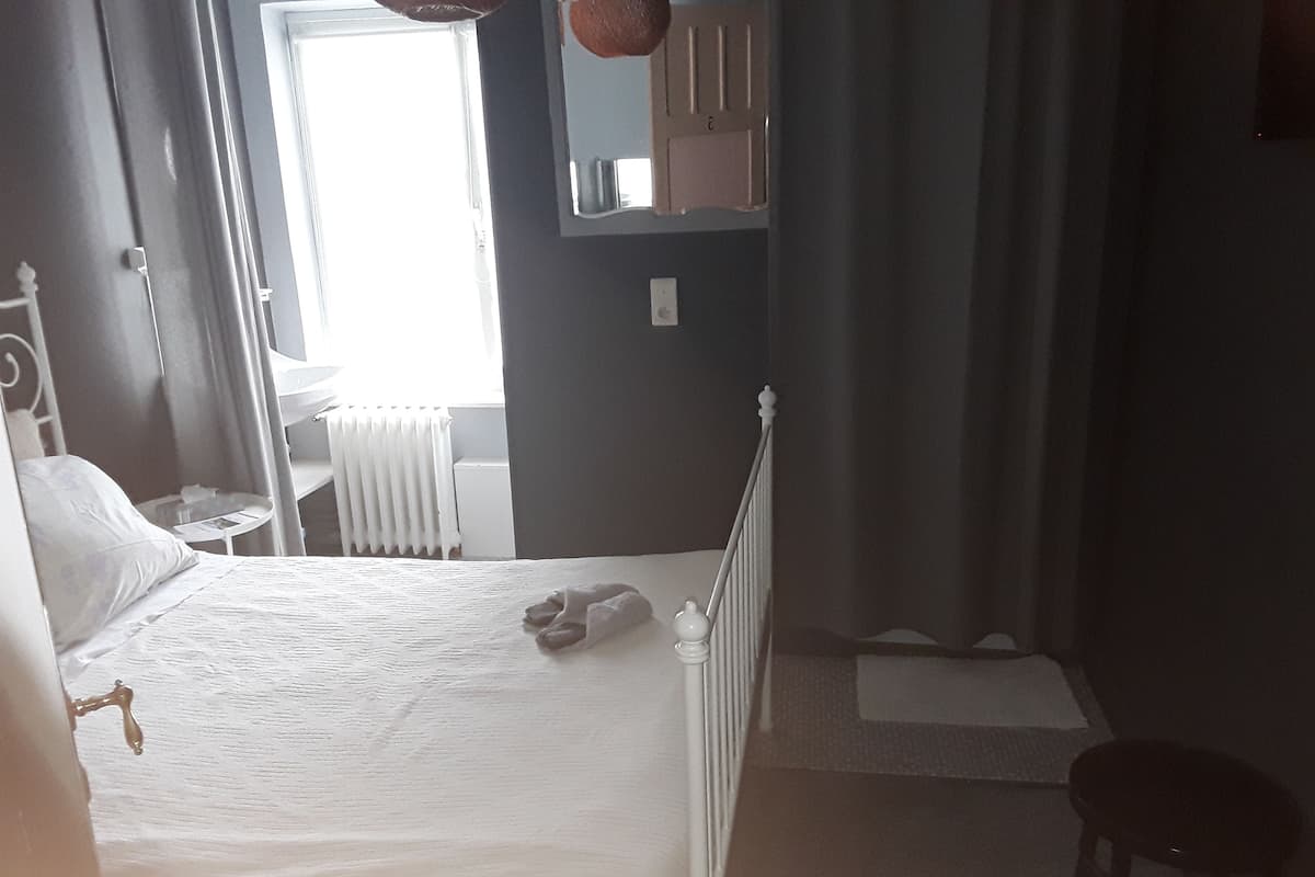 A bedroom with a bed, a chair, a radiator, and a window.