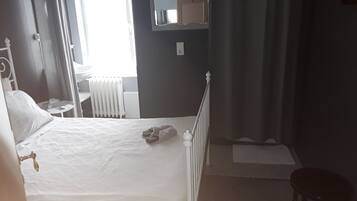 Un dormitorio con cama, una silla, un radiador y una ventana.