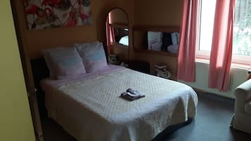 A bedroom with a bed, pillows, a bedside table, a mirror, and a window with curtains.