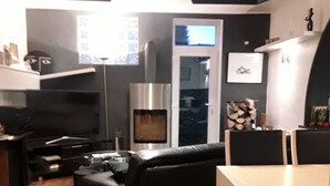 A modern living room with a black leather sofa, a wooden dining table, and a built-in fireplace.