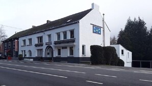 A two-story building with a white facade and a black roof. There is a sign with a blue background and white text on the side of the building.