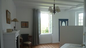 A room with a fireplace, a bed, a chair, a window with curtains, and a chandelier.