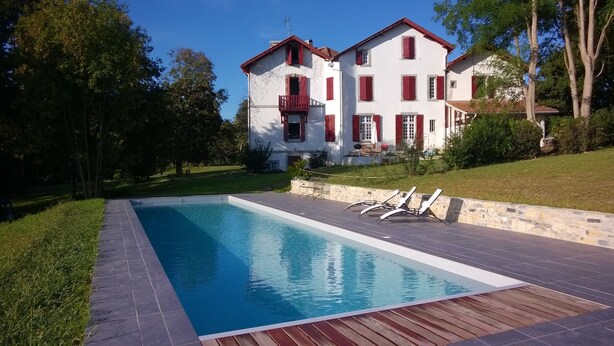 A rectangular swimming pool with a wooden deck and a stone wall.