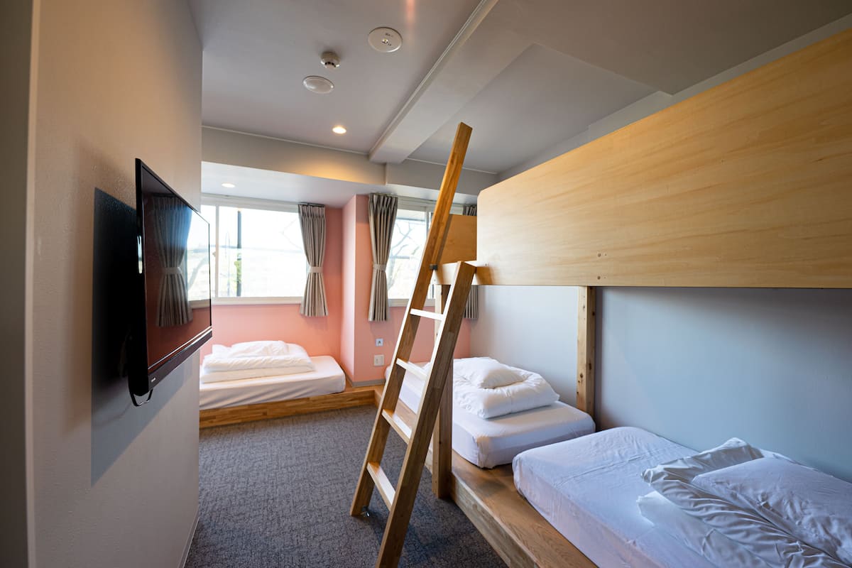 Une chambre avec des lits superposés, un téléviseur fixé au mur et une fenêtre avec des rideaux.