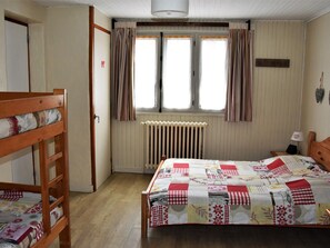 A bedroom with a wooden bunk bed, a quilted bedspread, a radiator, and a window with curtains.