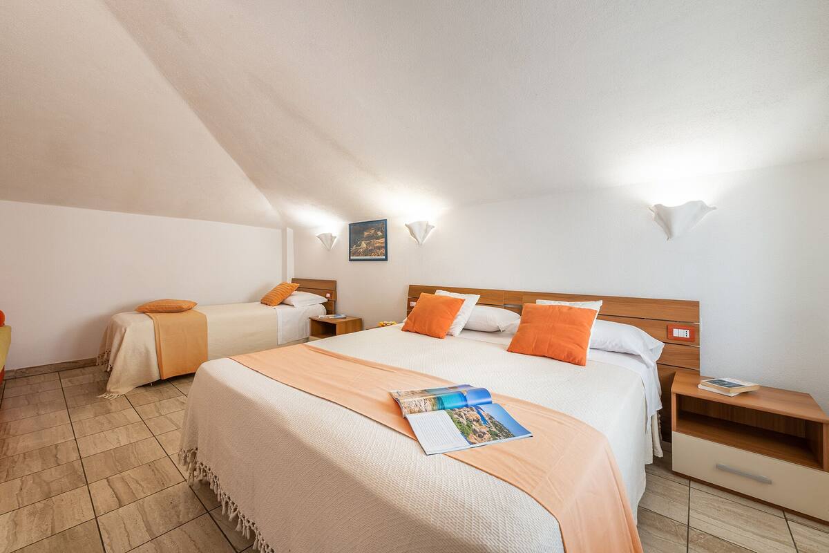 A hotel room with a large bed, two smaller beds, a wooden nightstand, and a bedside table.