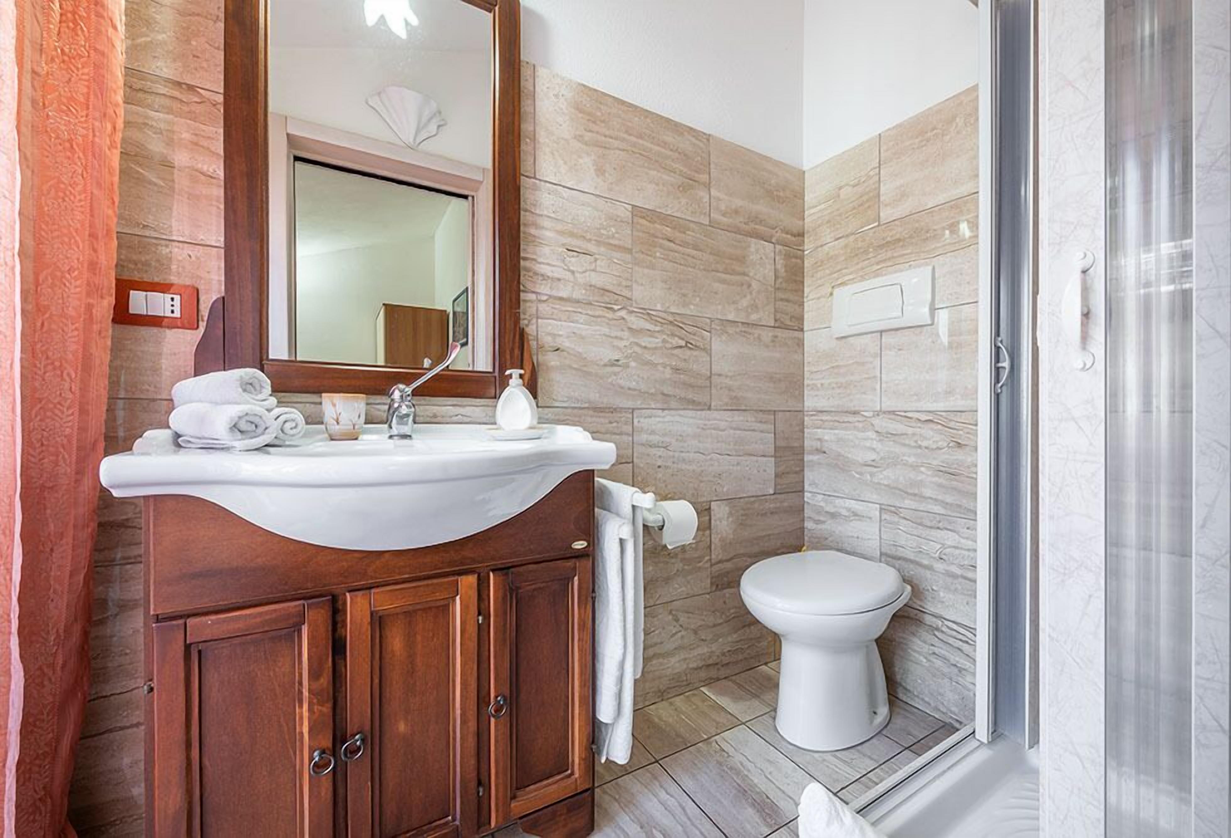 Een badkamer met een houten wastafelmeubel, een witte wasbak, een spiegel, een toilet en een douchehoek.