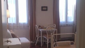 Ett hotellrum med en säng, ett litet bord och en stol. Det finns ett fönster med gardiner och en hängande lampa.