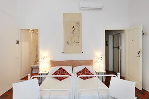 A double bed with a headboard, two bedside tables with lamps, a wall-mounted air conditioner, and a door to the right. - Lucretia House Affittacamere (Florence)