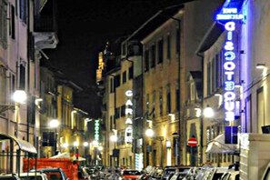 A street view at night with illuminated signs, including a 'Garage' sign, and parked cars along the sidewalk. - Lucretia House Affittacamere (Florence)