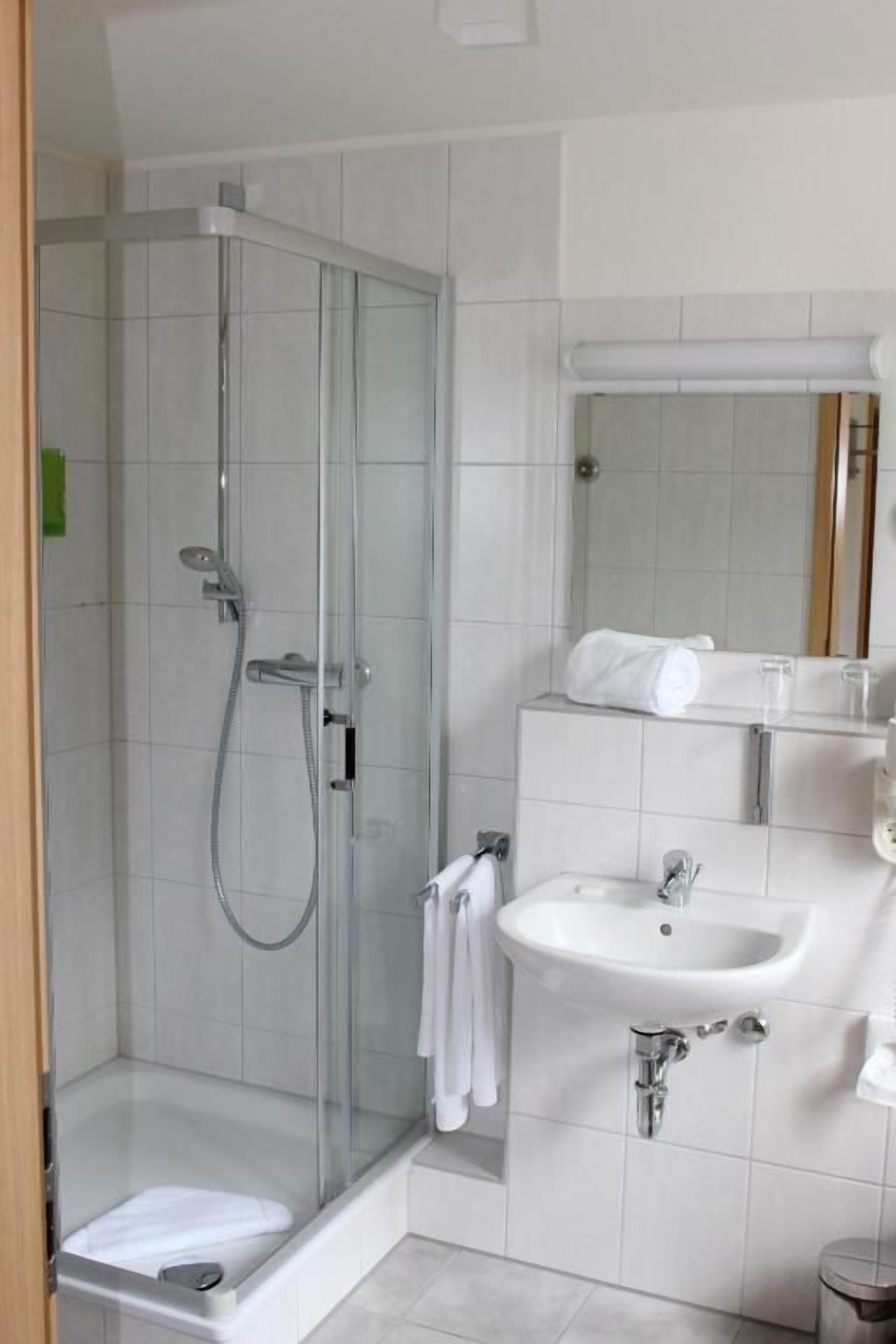 Een moderne badkamer met een douchecabine van glas, een witte wastafel en een spiegel boven de wastafel.