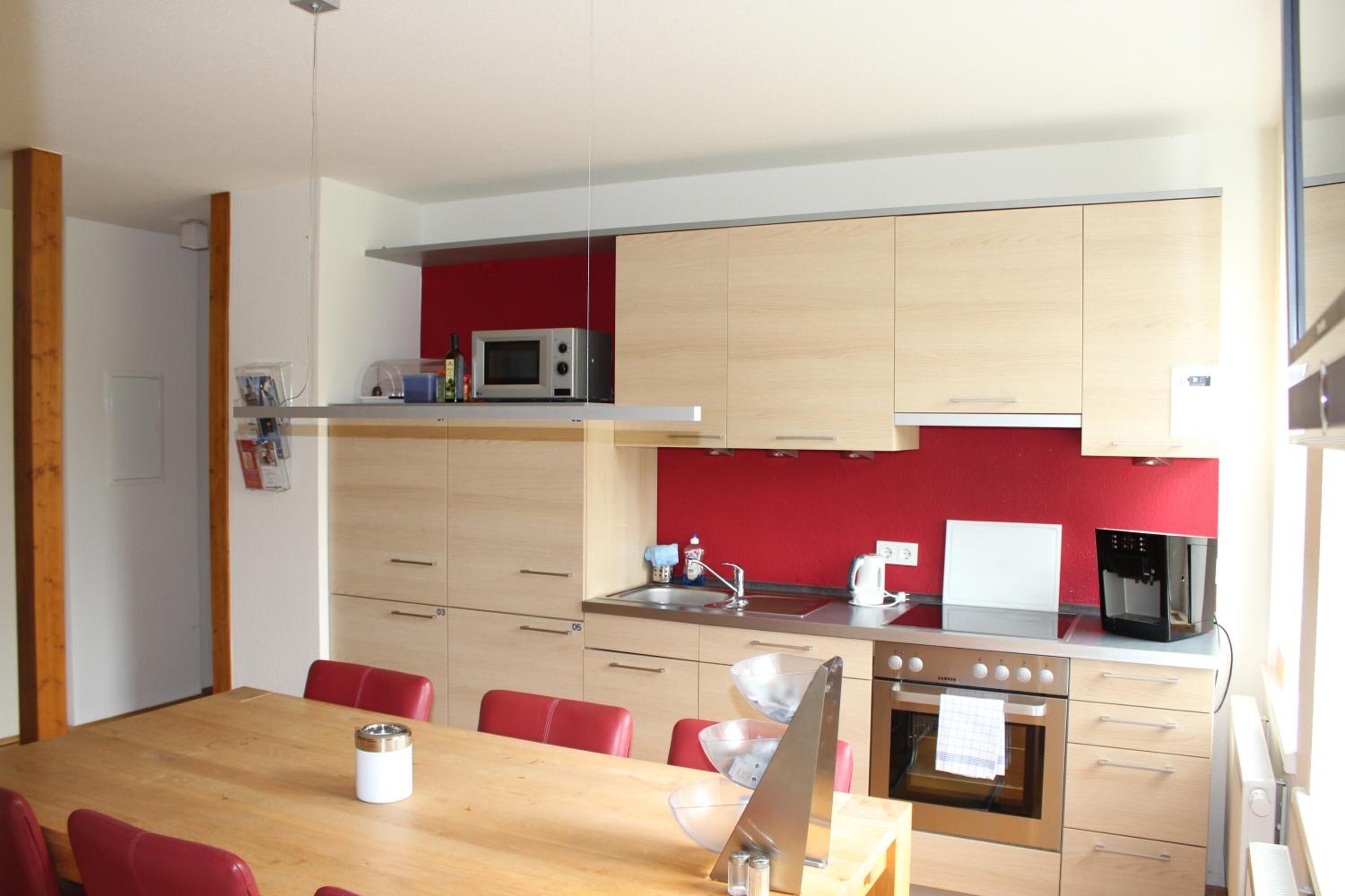 A compact kitchen with a microwave, stove, and red backsplash.