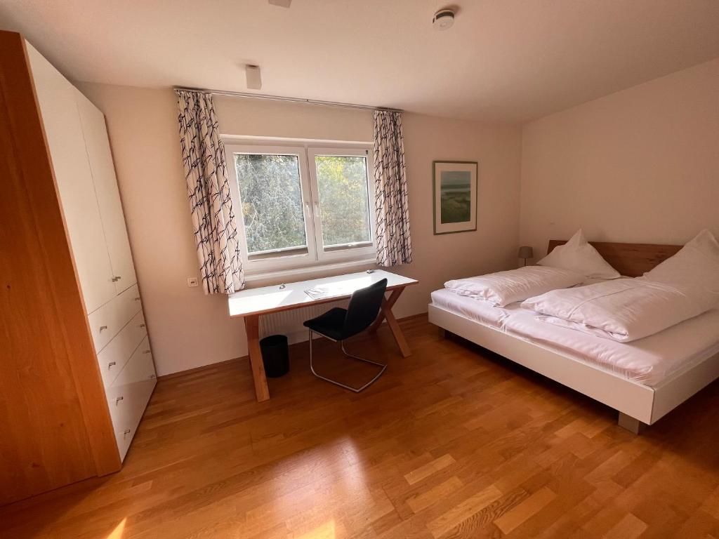 Ett sovrum med en säng, ett skrivbord med en stol, ett fönster med gardiner och ett element.