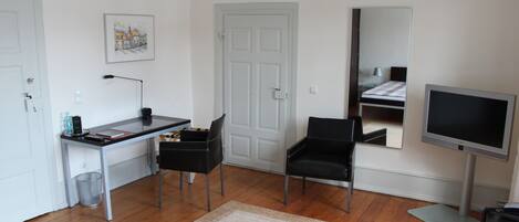 A room with a desk, two black chairs, a TV, a door, and a small rug.