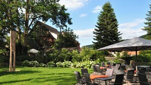 An outdoor patio with tables and chairs, surrounded by greenery and trees. - Poststation zum Alten Forstamt (Morschen)