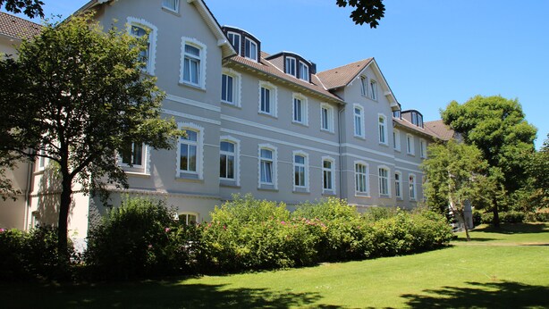 A multi-story building with a symmetrical facade, large windows, and a well-maintained lawn. - Comfortable, modern living in a central, quiet island location for 2 people (Wangerooge)