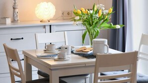 A dining table with white chairs, a vase with yellow tulips, a lit lamp, and a tray of cookies. - Comfortable, modern living in a central, quiet island location for 2 people (Wangerooge)